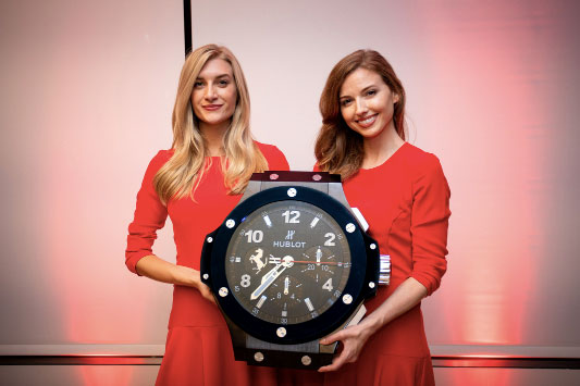 Models holding an oversized watch at the Ferrari Tailor Made opening